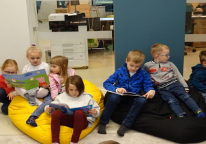 Dzieci siedzą na pufach, oglądają książki.